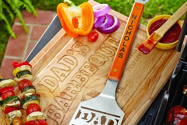 personalized cutting board and spatula with vegetable and meat skewers on top of a barbecue grill in back yard by grass lawn