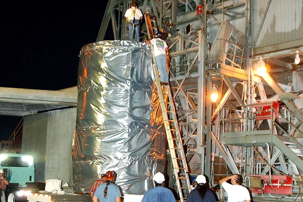 KENNEDY SPACE CENTER, FLA.  -  Before dawn, the Space Infrared Telescope Facility (SIRTF) is attached to an overhead crane that will lift it up the mobile service tower on Launch Pad 17-B, Cape Canaveral Air Force Station.  SIRTF will be attached to the Delta II rocket and encapsulated in its fairing before launch.   Consisting of three cryogenically cooled science instruments and an 0.85-meter telescope, SIRTF is one of NASA’s largest infrared telescopes to be launched.  It is the fourth and final element in NASA’s family of orbiting “Great Observatories.”  SIRTF will obtain images and spectra by detecting the infrared energy, or heat, radiated by objects in space. Most of this infrared radiation is blocked by the Earth's atmosphere and cannot be observed from the ground.