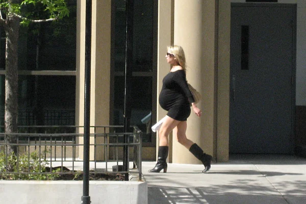 a very pregnant blond woman in a short, black dress struts down kinzie.