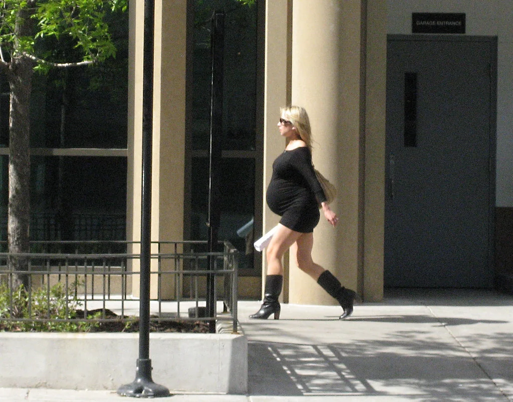 a very pregnant blond woman in a short, black dress struts down kinzie.
